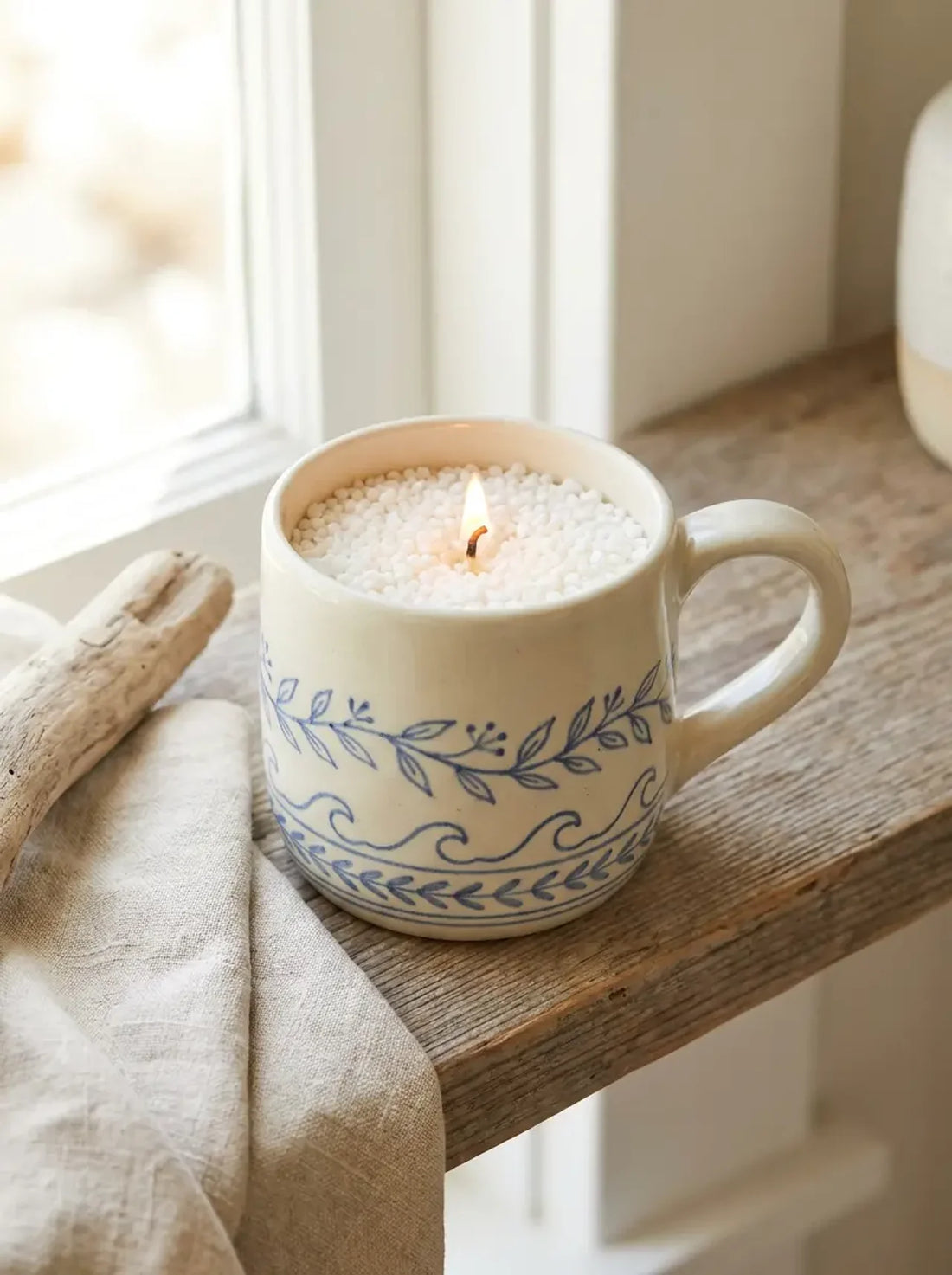 Hand-painted blue and white mug turned into a candle with White Cove candle sand and a lit cotton wick