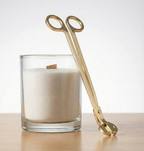 Premium candle accessories for sustainable home pearled wax by White Cove UK. A luxury gold wick cutter displayed next to a DIY refillable candle in a glass vessel on a light wood surface