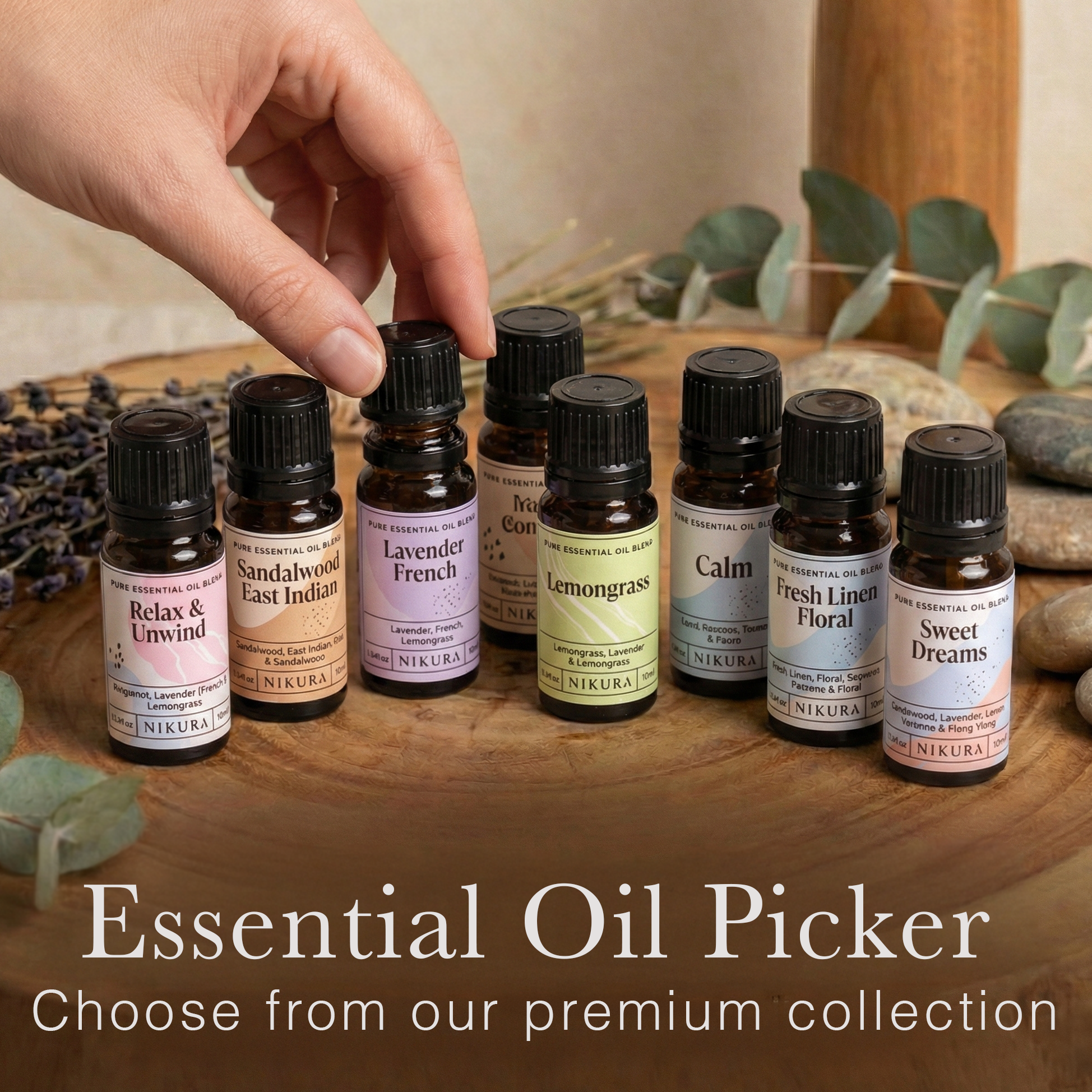 Eight bottles of 10ml Nikura essential oil blends, including Lavender and Lemongrass, styled with dried botanicals. A customer's hand reaches for a bottle to scent their White Cove refillable candle