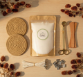 A luxury, sustainable refillable candle kit by White Cove UK. The comprehensive set features unscented plant-based candle sand, rustic coasters, and premium accessories including wooden wicks and a gold wick trimmer, arranged with natural botanicals
