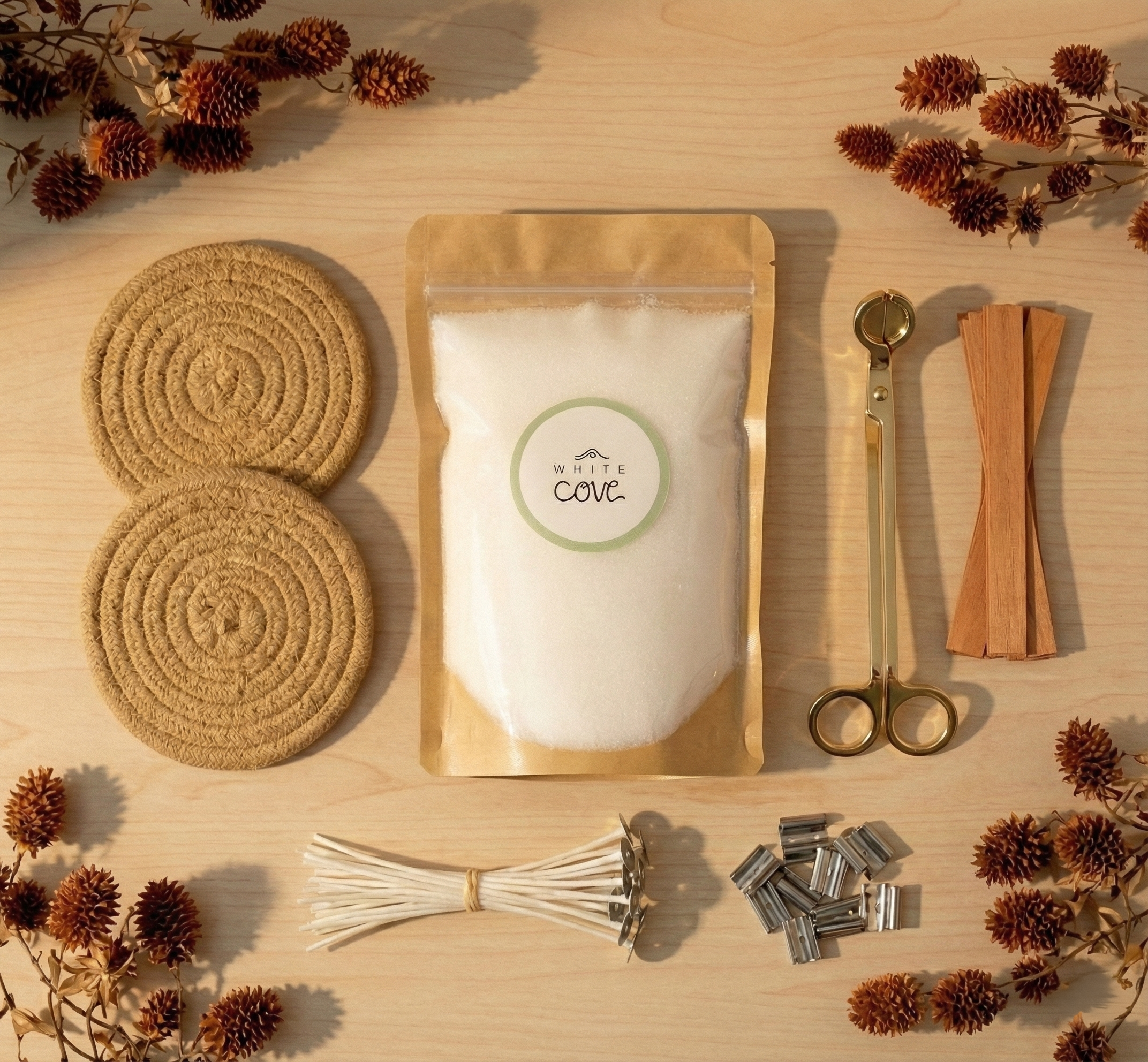 A luxury, sustainable refillable candle kit by White Cove UK. The comprehensive set features unscented plant-based candle sand, rustic coasters, and premium accessories including wooden wicks and a gold wick trimmer, arranged with natural botanicals