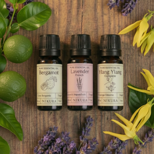 Premium essential oil bundle by White Cove UK featuring Nikura blends. Three amber glass bottles surrounded by fresh botanicals to represent the natural scent profiles used to customize Dorset-packed refillable candle sand