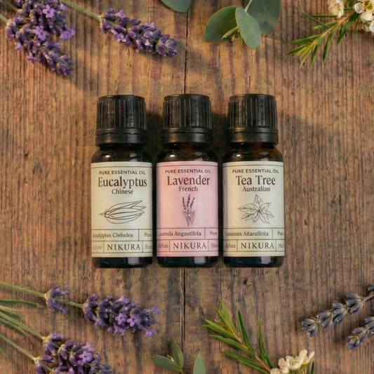 Premium wellness essential oil bundle by White Cove UK. Three amber glass bottles of Nikura pure essential oils surrounded by fresh botanicals, designed for scenting sustainable vegetable-based wax granules hand-packed in Dorset